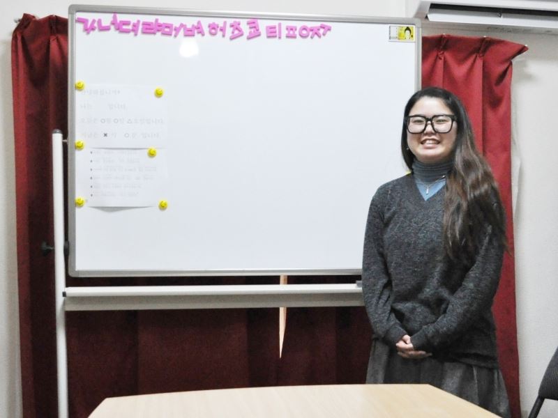 福岡市にある金舜華の韓国語教室の古賀先生が教室内のホワイトボードの前に座っている時に撮った写真。