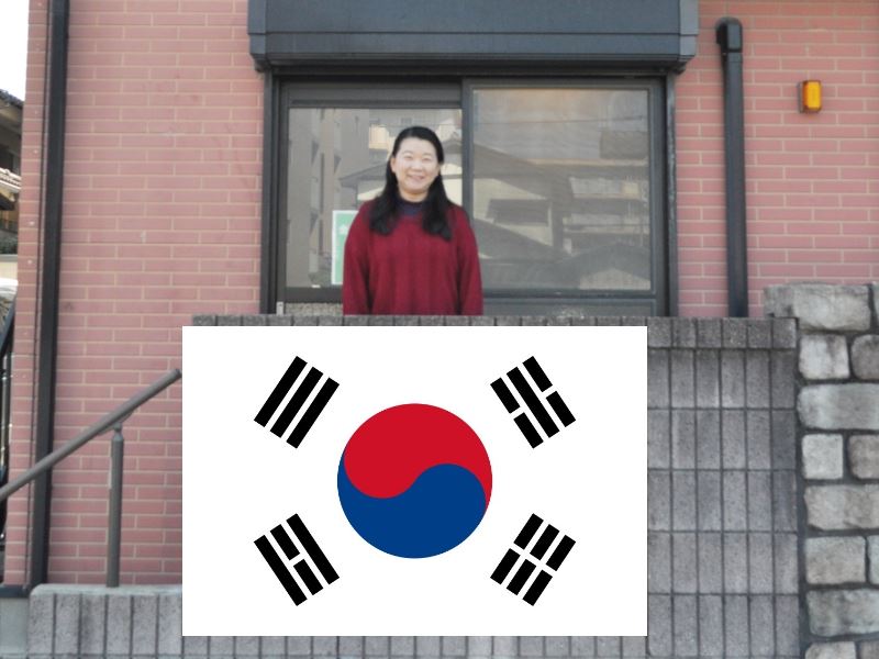 福岡市にある金舜華の韓国語教室の金舜華先生が教室の前の階段の上で立っている写真です。韓国の国旗の画像を写真に張り付けてます。